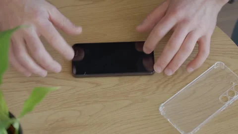 Man installing screen protector glass on smartphone on wooden table Stock Footage 330396489