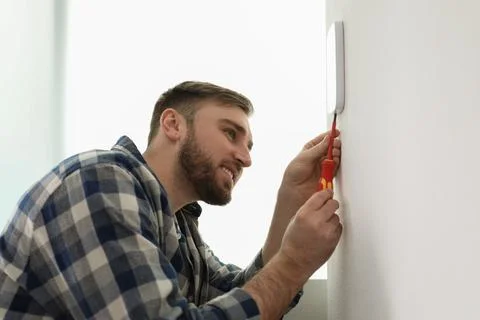 Man installing security alarm system on light wall at home Stock Photos