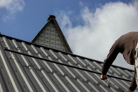 A man is installing solar panel mounts on the roof. Selective focus Stock Photos