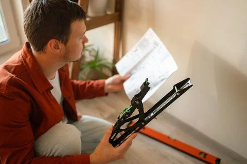 Man installing television wall mount, carefully reading instructions for home Fotos de archivo