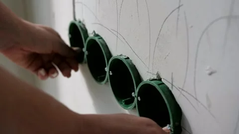 A man installs boxes for electrical outlets in pre-prepared holes in the wall Stock Footage 302285259