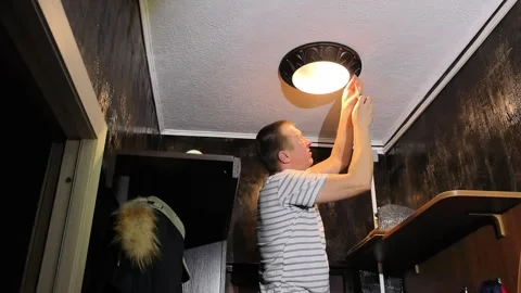 Man installs ceiling light fixture in room with dark walls during evening hours Stock Footage 330188578