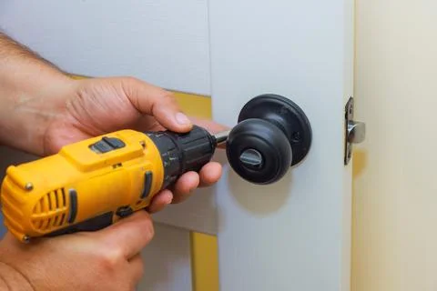 Man installs a door handle using a power drill in a home workshop during daytime Foto stock