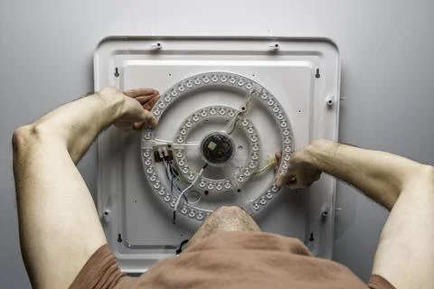 Man installs round LED ceiling light module during home repair, fixing wiring Photos
