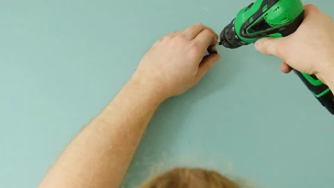 Man installs screw using electric screwdriver into plasterboard Stock Footage 304407891