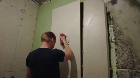 Man installs wall tiles in a construction site in the early afternoon using tool Stock-Footage 332506137