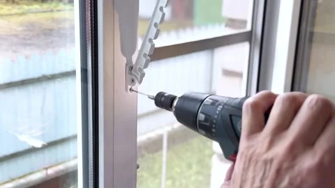 A man installs a window restrictor on his home using a screwdriver Stock Footage 297222208