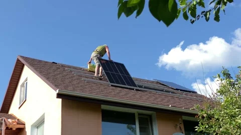Man instals solar panel on on bituminous tiles roof Stock Footage 203834654