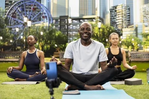 Man instructor meditating with open palms as women follow on mats Stock Photos
