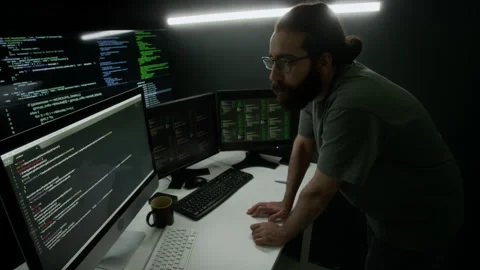 Man Intensely Studying Four Computer Monitors Displaying Lines of Code Stock Footage 302195104