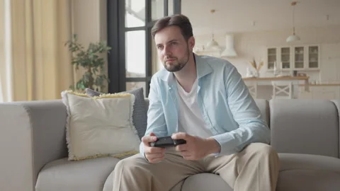 Man Intently Competing In Console Game On Sofa In Bright Modern Apartment 動画素材 311259705