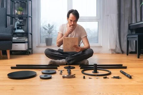 The man is intently studying the instructions for self-assembly of furniture. 스톡 사진