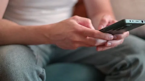 A man interacts with his smartphone while seated on a couch. The setting is 스톡 동영상 337111435