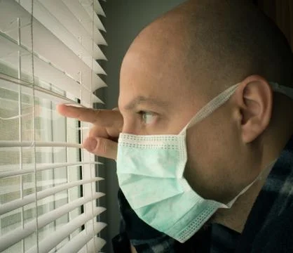 Man in isolation looking through window blinds Foto stock