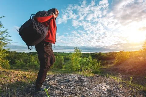A man in a jacket and with a backpack goes over a large stone at sunset Stock Photos