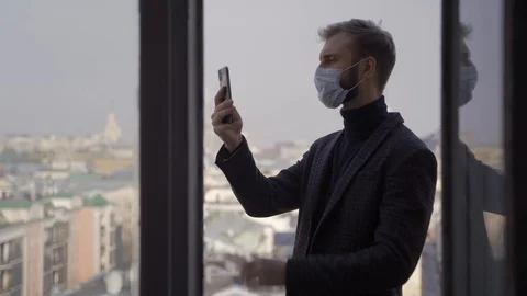A man in a jacket and mask speaks via video link on the balcony of a tall buildi Stock Footage 128360801