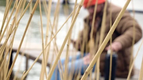 A man in a jacket and orange hat sits on a wooden jetty   Video stock 275132809