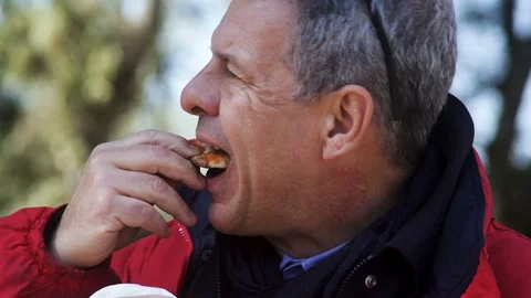 A man in a jacket with a big appetite eats a piece of pizza on the street Video stock 100940320