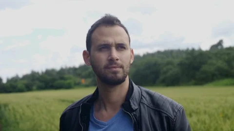 Man with a jacket looking serious in an empty country road with fields in bg Stock Footage 107263238