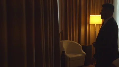 Man in jacket move curtains to look out the window in room of the hotel Stock Footage 121931519