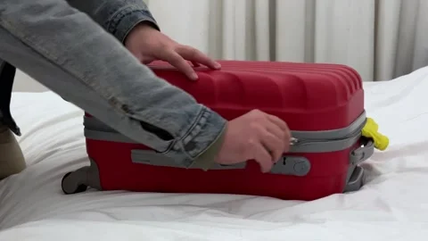 Man in jacket opens red suitcase on bed in hotel room puts t-shirt, shorts Video stock 300652137