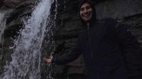 Man in Jacket Puts Hand in Waterfall Stock Footage 79736556