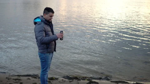A man in a jacket on the river bank throws a can into the river. Environmental Stock Footage 142894945