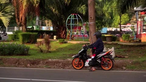 Man jacket sits on a motorcycle next to city park, Semarang, Central Java, Stock Footage 197404679