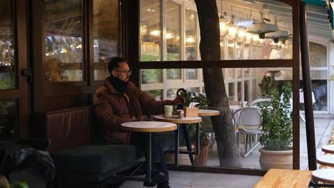 Man in a jacket sits on an open cafe terrace on an autumn day drinking matcha  스톡 사진