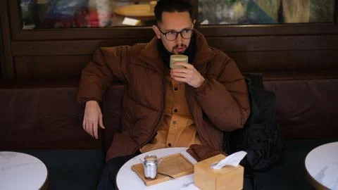Man in a jacket sits on an open cafe terrace on an autumn day drinking matcha  Fotos de archivo