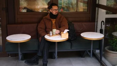 Man in a jacket sits on an open cafe terrace on an autumn day drinking matcha  Stock-Fotos