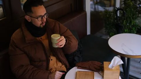 Man in a jacket sits on an open cafe terrace on an autumn day drinking matcha  Stock-Fotos