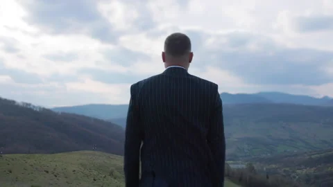 A man in a jacket stands against the beautiful landscape of the mountains with Stock Footage 164681668