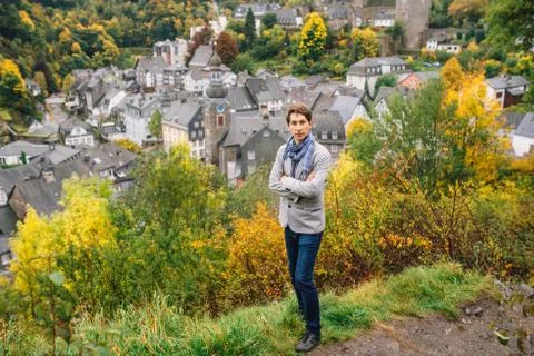 A man in a jacket stands against a panoramic view of Monschau, despite the we Stock Photos
