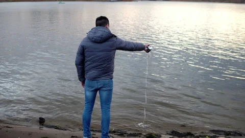 A man in a jacket stands on the banks of a river, lake and pours a drink into Video stock 142895405