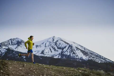 A man in jacket trail runs at dawn with mountains in the distance Stock Photos