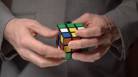 Man in a jacket is trying to collect the colors of a rubik's cube. Puzzle games Stock Footage 124428332