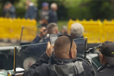 Man in jacket using smartphone while sitting in open car at outdoor event Stock Photos