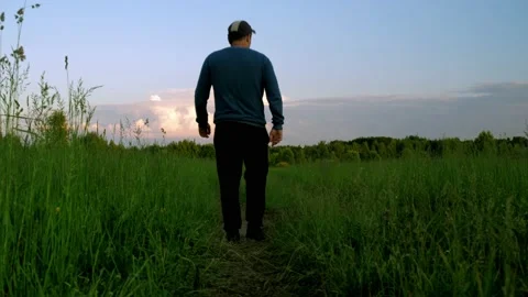 A man in a jacket is walking along a path in a green field. against the Stock Footage 160921005