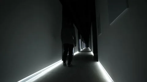 Man in a jacket walks along a long dark corridor with lights on the floor Stock Footage 205324895