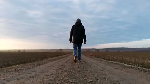 A man in jacket walks away in a straight line on a muddy endless road (60 FPS) Stock Footage 145843137