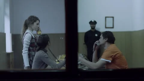 A man in jail talking on the phone with his wife and daughter and touching glass Stock Footage 283093198