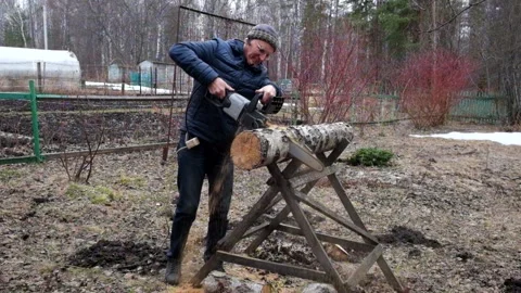A man in jeans saws a birch log with an electric saw outdoors Stock Footage 209225515