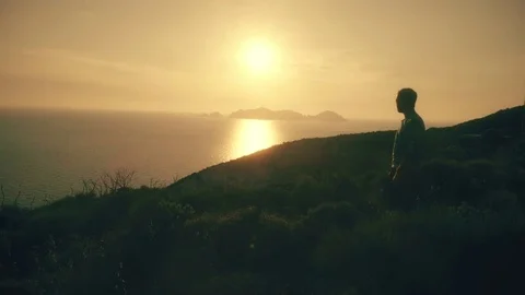 Man jogging along a trail on a hill with view of the ocean at sunset 스톡 동영상 77150675