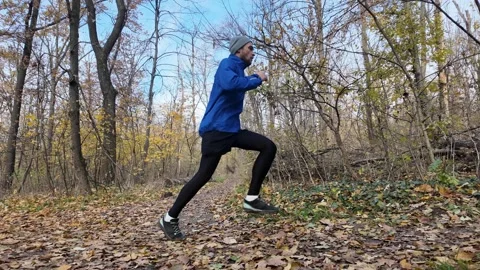 Man jogging and jumping over fallen tree in autumn forest, outdoor fitness Stock Footage 318175764