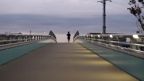 A man jogging away across an empty bridge Stock Footage 121401733