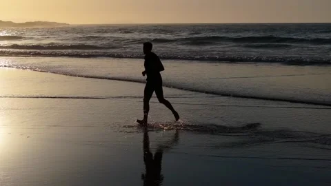 Man Jogging Barefoot On Wet Sandy Beach At Sunrise With Waves Rolling Stock Footage 310830200