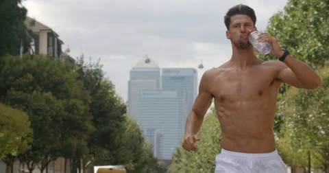 Man Jogging with Cityscape backdrop takes a sip from a water bottle. Vídeo Stock 68124548