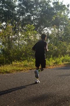 Man Jogging on Road Surrounded by Trees 스톡 사진