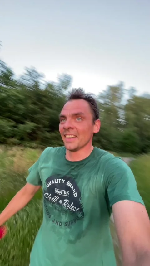 Man jogging selfie on meadow path at sunset with joyful expression and sweat Stock Footage 344583723